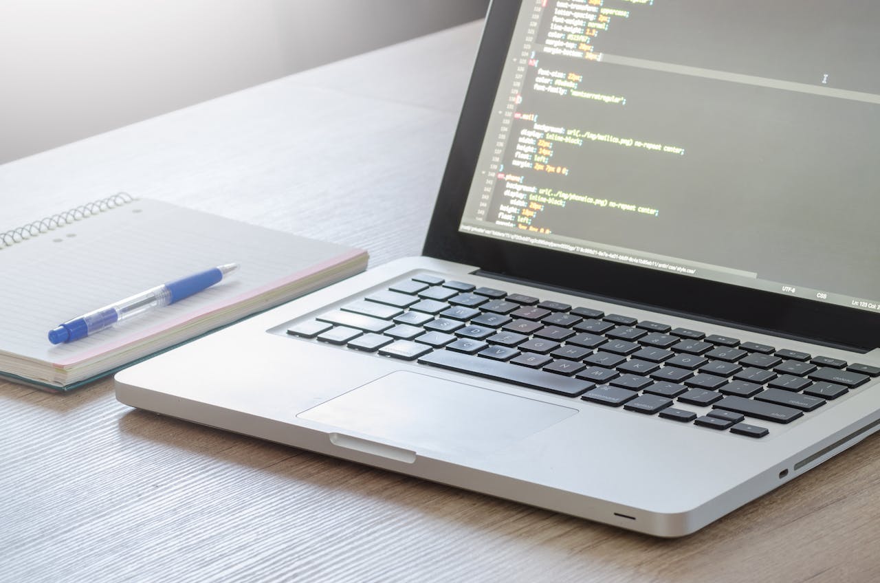pexels-photo-574073 Laptop with code editor open, notebook and pen on wooden desk, perfect for tech and work themes.